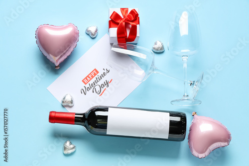 Bottle of wine with glasses, postcard and decor on blue background. Valentine's Day celebration