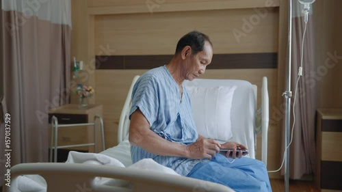 Sick old man using smartphone to call relatives with longing while sitting on bed looking at window inside hospital in lonely, depressed and hopeless attitude, health concept.