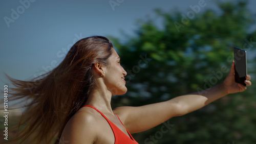 Happy young woman taking a selfie on a summer day, hair blowing in the wind, enjoying the sunny weather