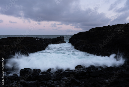 Wave splashing on a rocky coastal scene on the Hawaiian island of Kauai at sunset - long exposure
