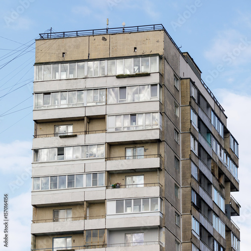 Detailed view of a concrete residential high-rise with enclosed balconies and signs of aging, set against a clear blue sky.