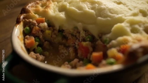 Close up of a steaming shepherd's pie with mashed potatoes and vegetables on a wooden surface
