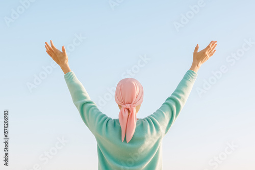 Woman with headscarf raising her arms to a clear, bright sky with a soft gradient evoking hope and positivity