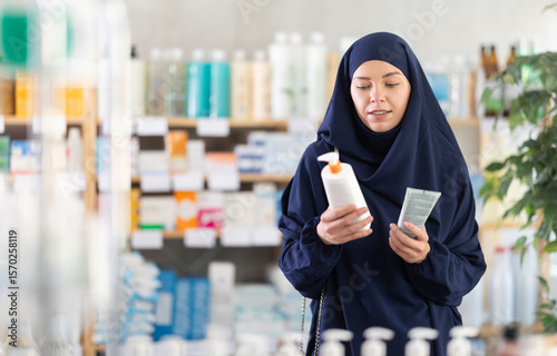 Photography Uncertain young female customer trying to choose cream in chemist's shop