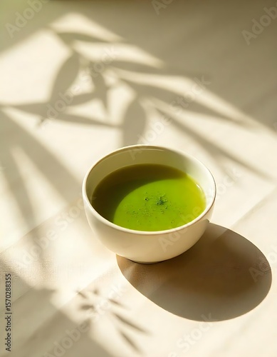 Serene Matcha Tea in Sunlight A Bowl of vibrant green matcha tea sits on a light beige surface bathed in sunlight dappled with leaf shadows.