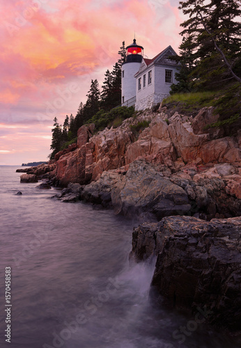 Bass Harbor Lighthouse illuminated at sunset with dramatic rocks and Atlantic Ocean on the foreground, Acadia National Park, Maine, USA