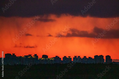 The fiery hues of a sunset illuminate the outlines of buildings against a darkening sky