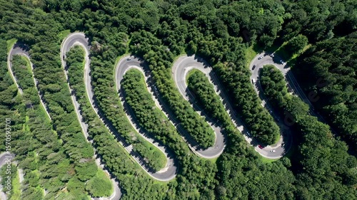 Flying over winding serpentine forest road with passing cars aerial slow motion view