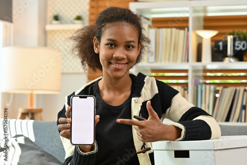 Young African Woman Pointing to Smartphone Screen with Delivery App or Online Shopping App at home