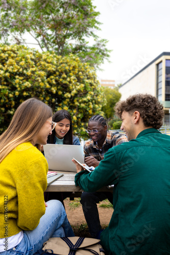 University students collaborating on project outdoors using laptop and tablet