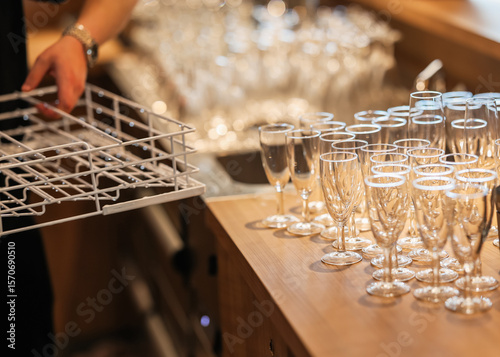 Clean drinking glasses arranged on counter next to a dishwasher rack in a restaurant kitchen. Preparation scene before service, no recognizable people.
