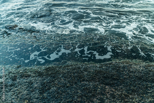 Closeup shot of foams created by the ocean waves meet a rocky shoreline.