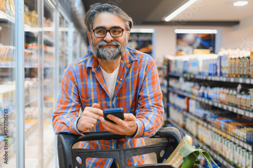 Senior Man doing grocery shopping at the supermarket, he is using apps on his smartphone