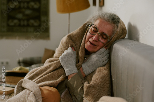 Canvas Print Senior Caucasian woman sitting on couch wrapping herself in blanket, wearing gla