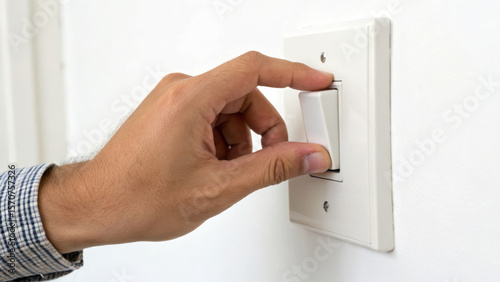 Hand switching on a light switch against a white wall.