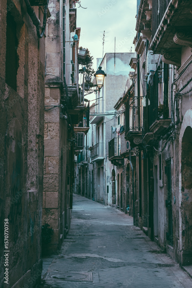 Fototapeta premium Narrow alleyway with warm street lamp in historic Syracuse, Sicily