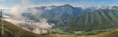 Mountain valley with river in the morning light, mist and green of forests and meadows, panoramic view	