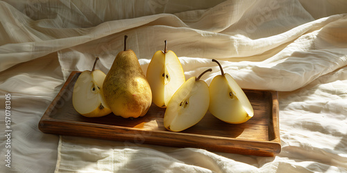 Fresh pears on wooden tray with one cut open on white cloth

