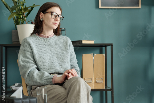 Cuadro en lienzo Woman sitting with hands clasped, wearing glasses, looking away thoughtfully dur