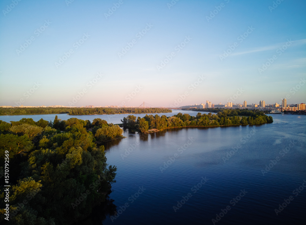 Fototapeta premium Scenic Riverside View With Lush Greenery and Urban Skyline in the Distance