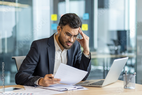 A concerned businessman reviews documents in his office, displaying stress and concentration as he faces a challenge.