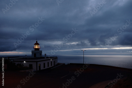 Coastal Lighthouse Illuminated at Dusk Under Moody Sky Overlooking the Ocean