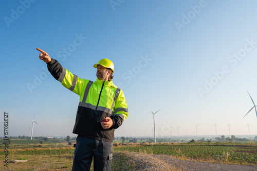 Engineer wearing uniform inspection and survey work in wind turbine farms rotation to generate electricity energy. Maintenance engineer working in wind turbine farm at sunset.
