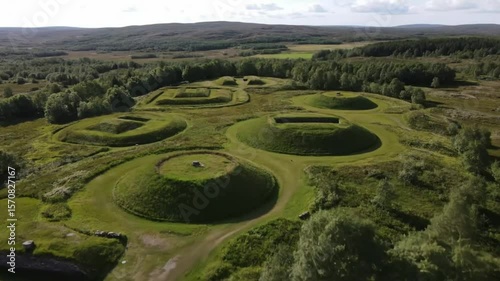 An aerial view captures the ancient burial mounds and barrows scattered across the green landscape of norway, a historical viking heritage site