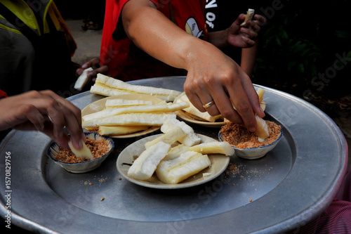 Hands hold steamed cassava dip into sesame salt before eating. This adds a subtle sweetness and nutty aroma to the cassava.
