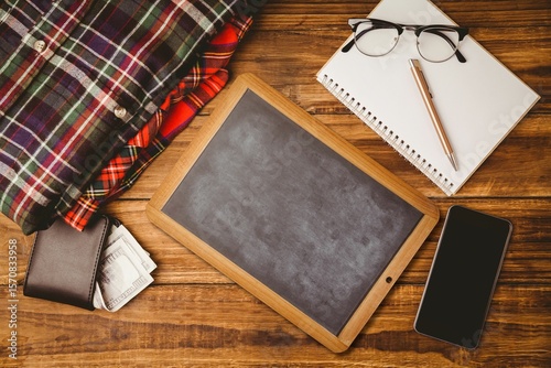 Small blank chalkboard is sitting in flat-lay arrangement, with shirts, wallet, notebook with pen