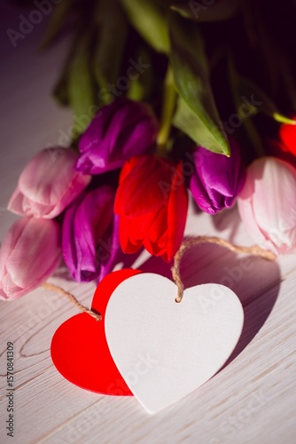 Colorful tulip bouquet is being shown in flat design on pale wooden surface with heart tags