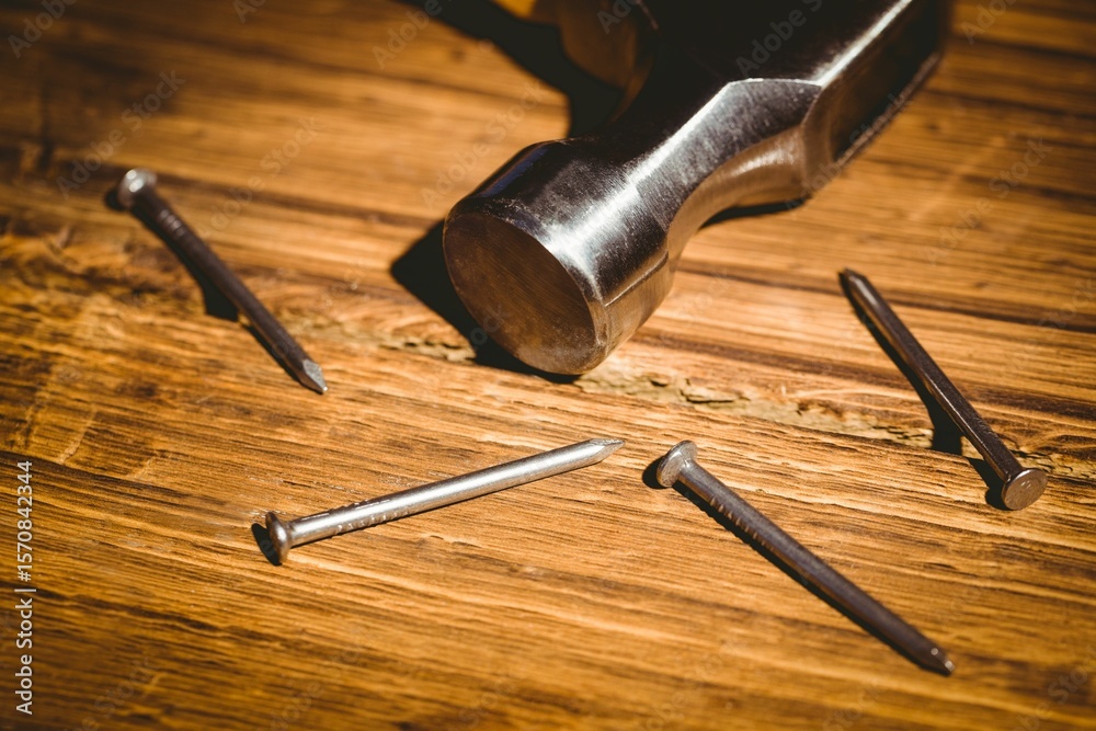 Obraz premium Flat design is showing metallic hammer head resting on warm wood surface with scattered steel nails