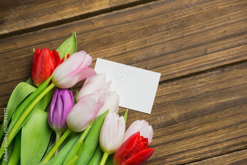 Multicolored tulip bouquet is being shown in flat design on plank tabletop with blank white card