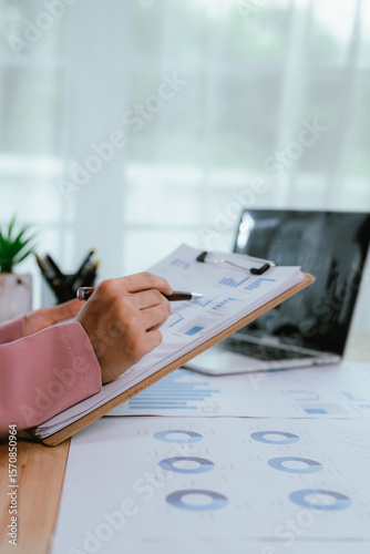 Photography Businesswoman in pink coat working at desk using smartphone and laptop, managing tasks and planning projects in modern and organized office environment