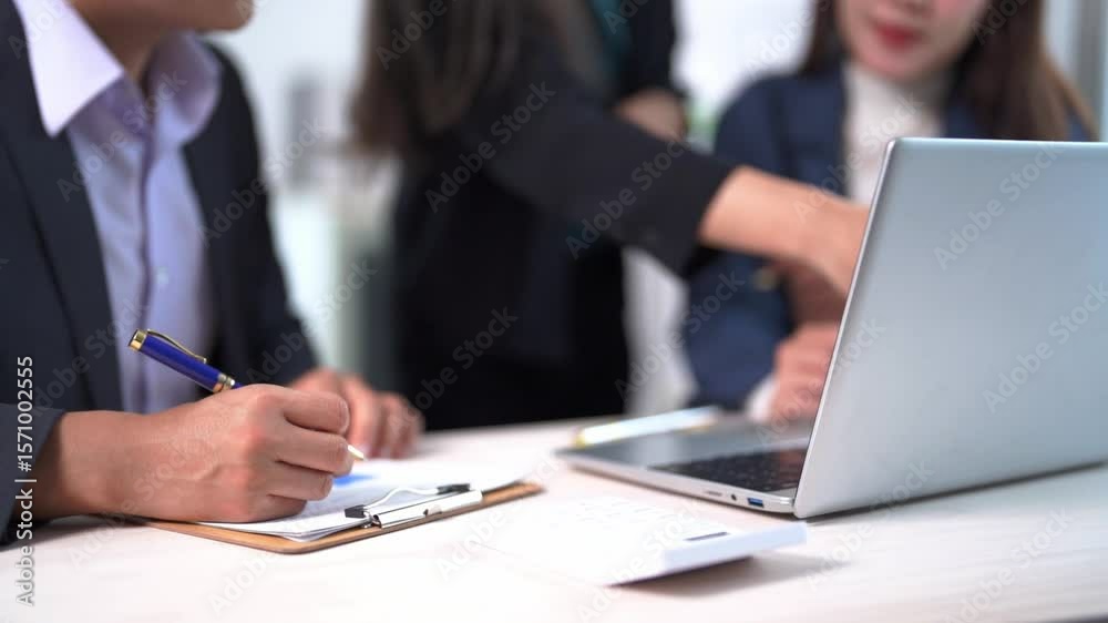 A woman is writing on a clipboard with a pen. She is sitting at a desk with a laptop in front of her A woman is writing on a clipboard with a pen. She is sitting at a desk with a laptop in front of her