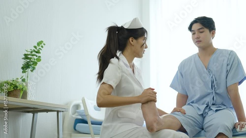 Healthcare professional nurse assisting young man during rehabilitation therapy, holding and stretching patient’s leg to assess recovery progress from injury, physical strain, or muscle weakness.
