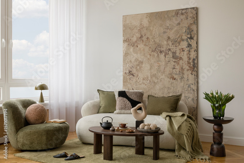 Elegant neutral living room with white sofa, olive green pillow, yellow spring flowers in a vase and ceramic accessories on a wooden table.