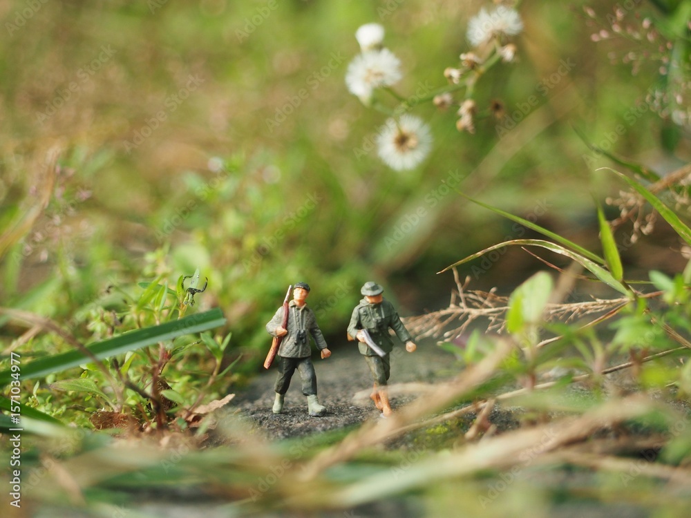 Obraz premium Mini toy of action figure at outdoor with blurred background. Toy photography concept design. Minifigure of hunter man character at forest with weapon, hat and face mask