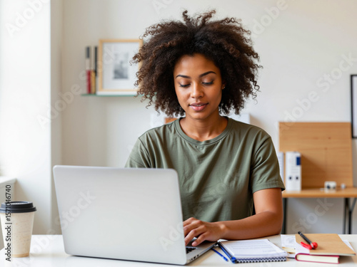 Young Black woman working on laptop at home desk with notebook  