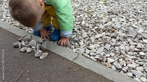 Young boy playing with gravel stones on outdoor pathway  