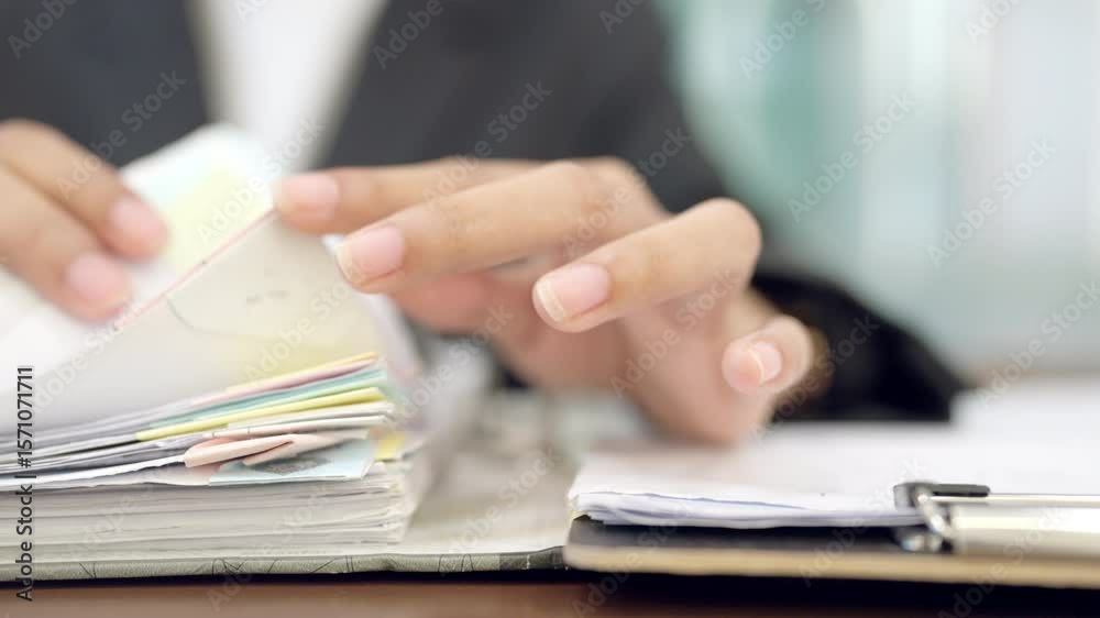 A person is looking at a stack of papers. The papers are in a folder and the folder is on a desk