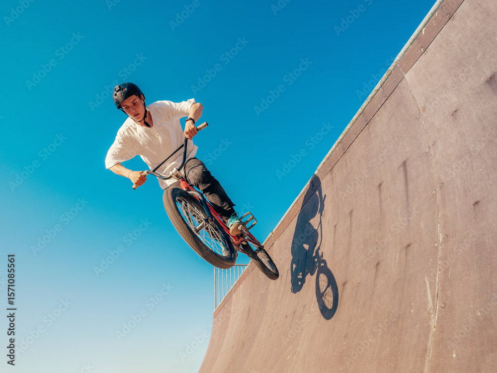 Fototapeta premium BMX bicycle rider flying and doing stunt in wooden quarter half-pipe. Skilled BMX freestyler athlete jumping over quarter ramp and doing aerial trick in street wooden half-pipe ramp park outdoors.