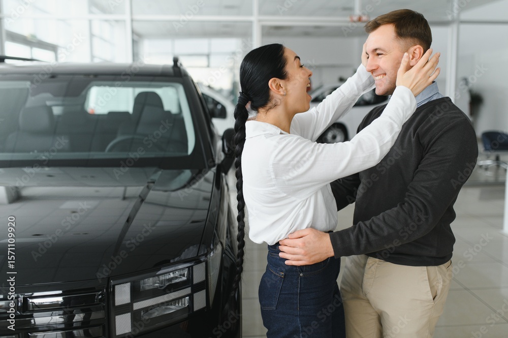 Beautiful young couple at car showroom exited because of buying a new car Beautiful young couple at car showroom exited because of buying a new car