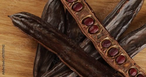 Carob pods on a wooden board top view, on a rotating table.