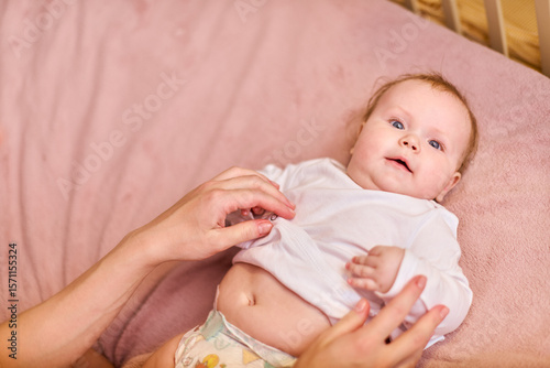Young woman with brown braids, caucasian, showing affection to baby girl on pink bed. Warm lighting enhances tender moment. Close-up captures smiles, bonding
