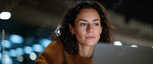 Focused woman engaged in latenight work on laptop in dimly lit modern setting