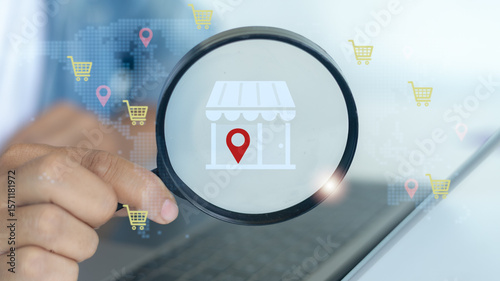 Hand holding magnifying glass focusing on local store icon with location pin, representing e-commerce growth, online shopping, and local business search.