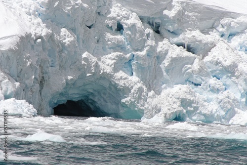 Glacier cave opening into icy sea.  Vast, white ice formations, a dark, frigid cave, and choppy water surround it