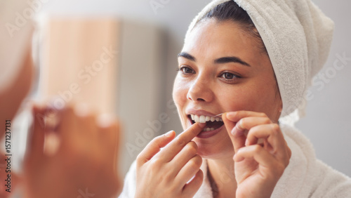 Fotografie Young woman flossing her teeth in front of mirror