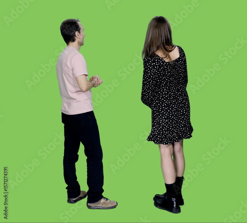 Back view of adult man in casual wear something explaining to young woman in black polka-dot dress on green chroma key background